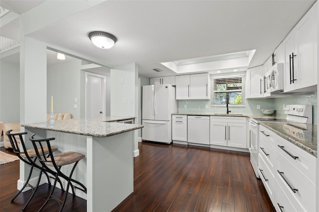 2033 Arbor Dr, Clearwater, FL 33760 - kitchen with white appliances, a breakfast bar, a tray ceiling, light stone counters, and dark wood-style flooring