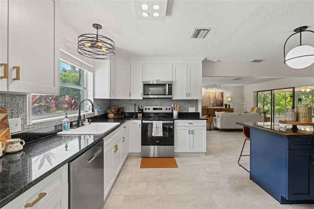 kitchen with appliances with stainless steel finishes, a sink, white cabinetry, open floor plan, and a textured ceiling