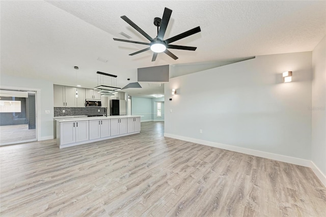 3330 46th Ter E, Bradenton, FL 34203 - unfurnished living room featuring light wood-style flooring, baseboards, a ceiling fan, a textured ceiling, and a sink