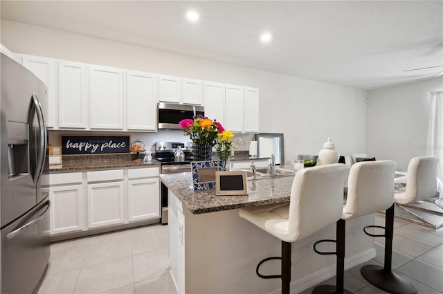 32965 Kaloko Rd, Wesley Chapel, FL 33543 - kitchen featuring stainless steel appliances, white cabinetry, a kitchen breakfast bar, dark stone counters, and a kitchen island with sink