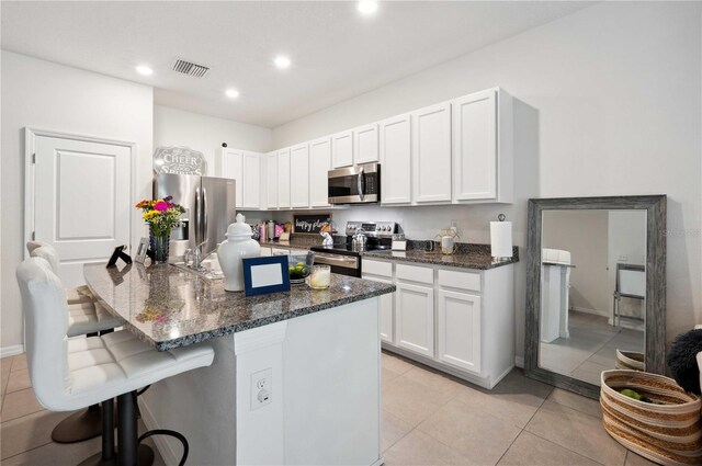 32965 Kaloko Rd, Wesley Chapel, FL 33543 - kitchen featuring stainless steel appliances, a breakfast bar area, dark stone countertops, light tile patterned flooring, and white cabinets
