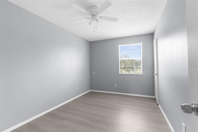unfurnished room with wood finished floors, a ceiling fan, a textured ceiling, and baseboards