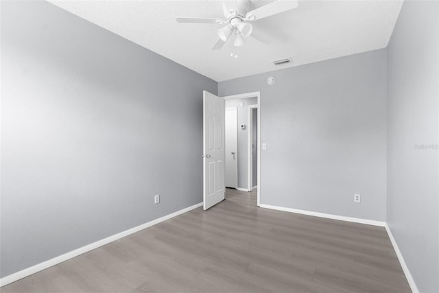 unfurnished room with ceiling fan, wood finished floors, baseboards, and a textured ceiling