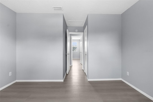 corridor with attic access, wood finished floors, baseboards, and a textured ceiling
