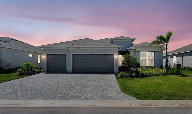 8589 Saint Kitts Cir, Englewood, FL 34224 - view of front of house featuring a garage, decorative driveway, a yard, stucco siding, and central AC