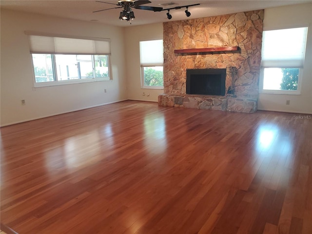 50 Water Oak Way, Oldsmar, FL 34677 - unfurnished living room with rail lighting, a ceiling fan, a stone fireplace, wood finished floors, and baseboards