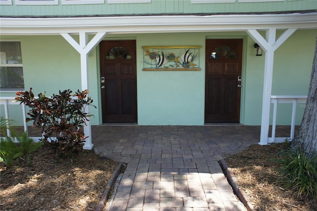view of exterior entry featuring covered porch and stucco siding