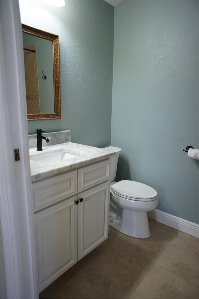 bathroom with toilet, vanity, baseboards, and a textured wall