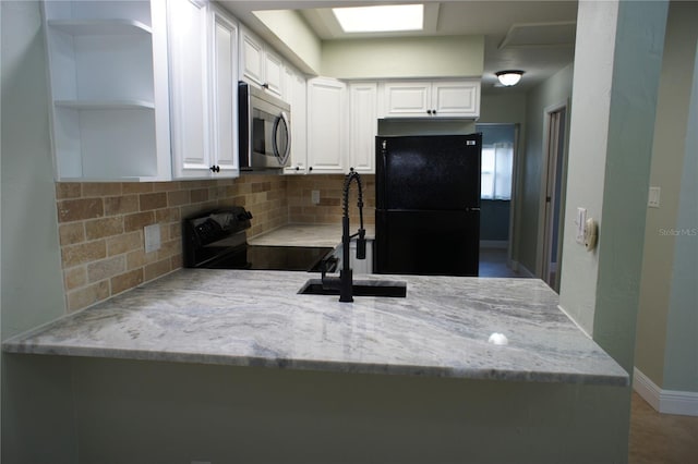 kitchen with black appliances, a peninsula, a sink, light stone countertops, and decorative backsplash
