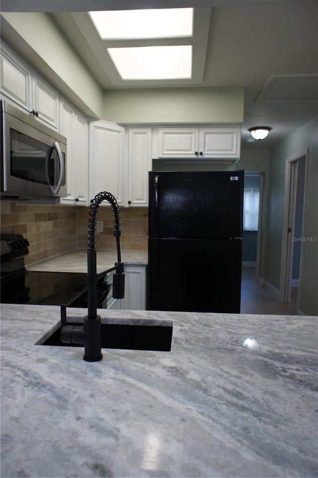 kitchen with black appliances, white cabinets, tasteful backsplash, a sink, and light stone counters