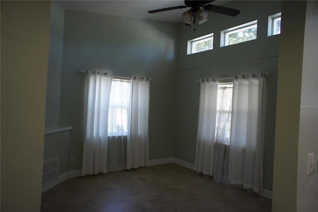 empty room featuring a ceiling fan, a high ceiling, and baseboards