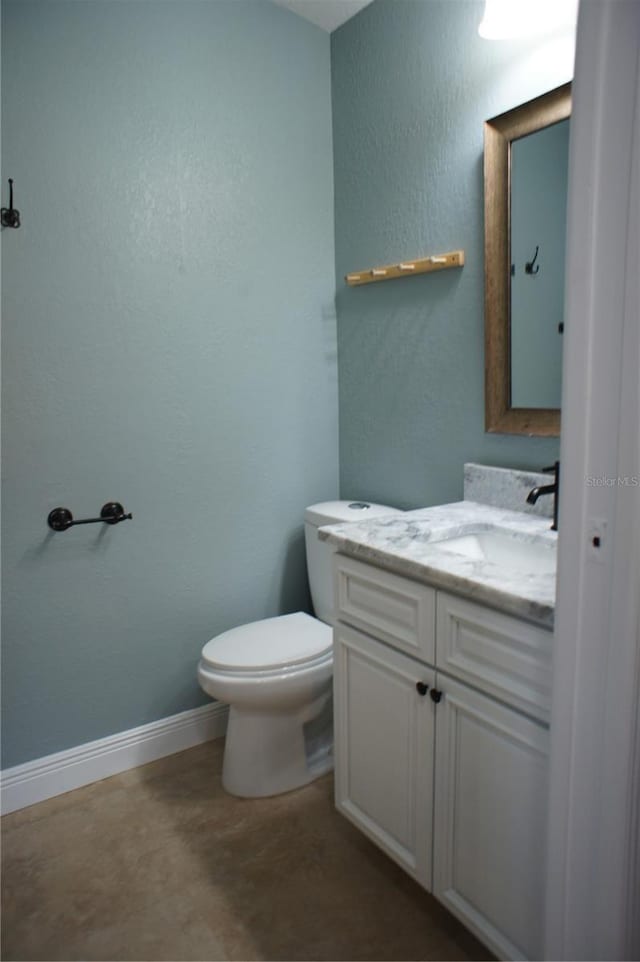 half bath with toilet, vanity, baseboards, and concrete flooring