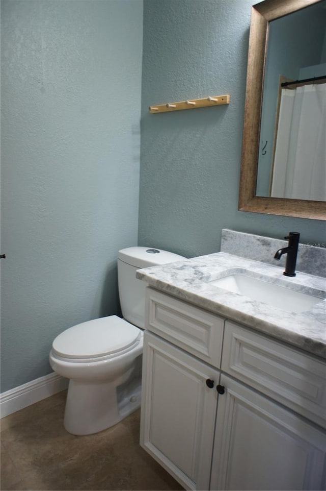 bathroom featuring toilet, vanity, baseboards, and a textured wall