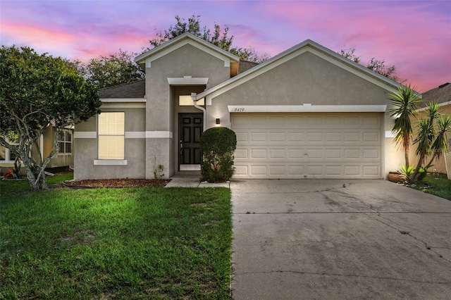 view of front facade with stucco siding, an attached garage, driveway, and a yard