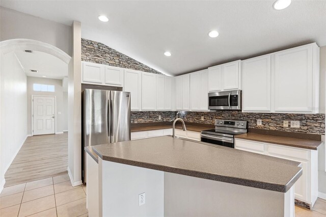 kitchen with stainless steel appliances, arched walkways, dark countertops, decorative backsplash, and light tile patterned floors