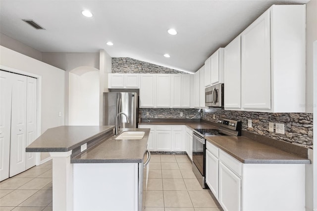 kitchen with appliances with stainless steel finishes, a sink, dark countertops, vaulted ceiling, and light tile patterned floors
