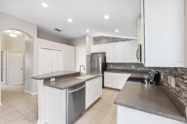 kitchen with stainless steel appliances, dark countertops, light tile patterned flooring, arched walkways, and a sink