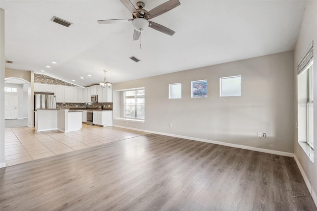 unfurnished living room featuring vaulted ceiling, light wood-style floors, ceiling fan, arched walkways, and a chandelier