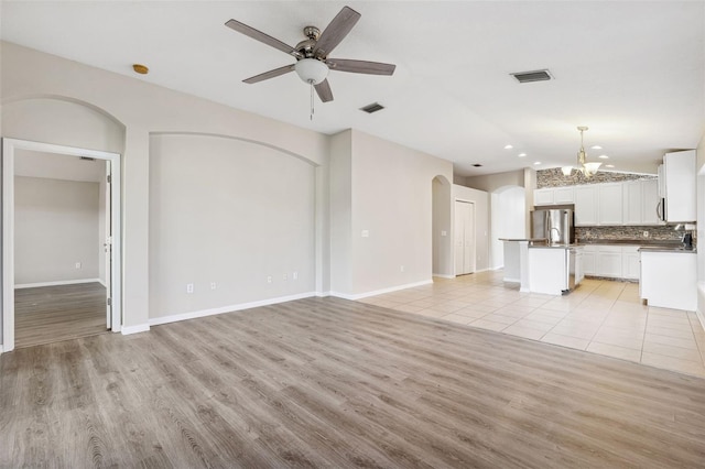 unfurnished living room featuring a chandelier, arched walkways, light wood-type flooring, vaulted ceiling, and a ceiling fan