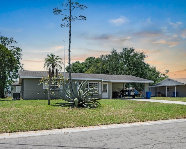 single story home with concrete driveway, a carport, central AC, and a yard