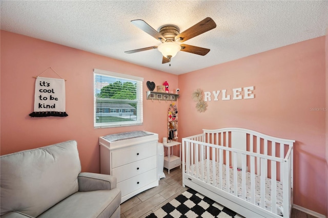 8497 Portulaca Ave, Seminole, FL 33777 - bedroom featuring a textured ceiling, ceiling fan, light wood-style floors, and a crib