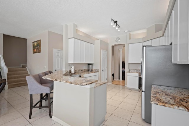 kitchen with freestanding refrigerator, a sink, a peninsula, light tile patterned floors, and light stone countertops