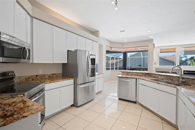 kitchen with appliances with stainless steel finishes, a sink, healthy amount of natural light, a textured ceiling, and stone countertops