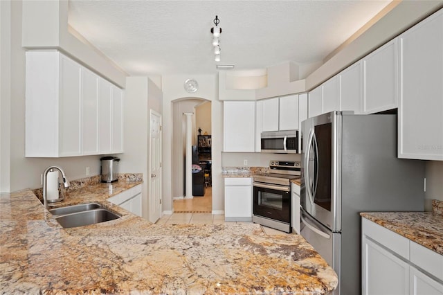 kitchen featuring appliances with stainless steel finishes, a sink, arched walkways, white cabinetry, and a textured ceiling