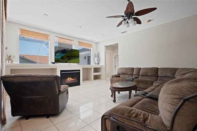 living area featuring light tile patterned floors, ceiling fan, a glass covered fireplace, and a textured ceiling