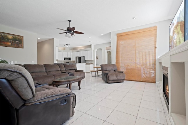 living area featuring a ceiling fan, a glass covered fireplace, light tile patterned floors, and recessed lighting
