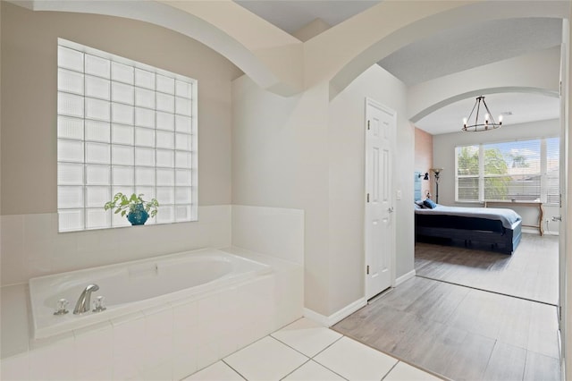 bathroom featuring connected bathroom, a bath, a chandelier, and baseboards