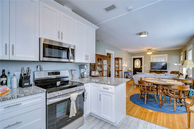 902 W Columbus Dr, Tampa, FL 33602 - kitchen featuring stainless steel appliances, open floor plan, a peninsula, white cabinetry, and light stone counters
