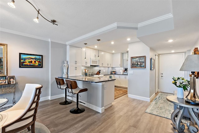 700 Beach Dr NE Unit 704, Saint Petersburg, FL 33701 - kitchen featuring white microwave, dark countertops, a peninsula, crown molding, and white cabinetry