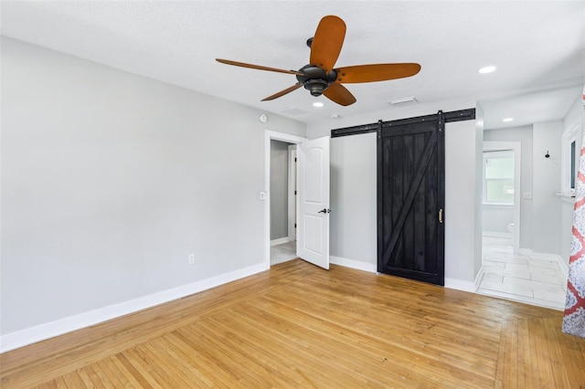 5632 Indiana Ave, New Port Richey, FL 34652 - unfurnished bedroom featuring a barn door, light wood-style flooring, baseboards, recessed lighting, and ceiling fan