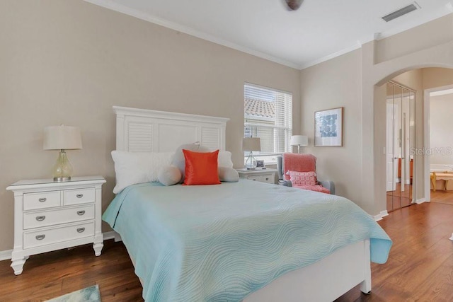 bedroom featuring arched walkways, wood finished floors, crown molding, and baseboards