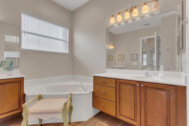full bath featuring a garden tub, two vanities, and wood finished floors