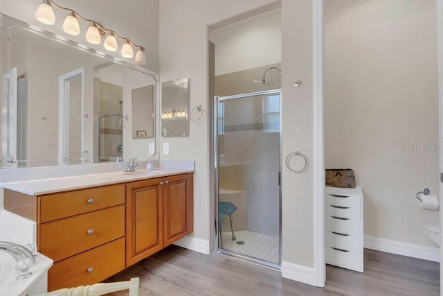 bathroom with a stall shower, wood finished floors, vanity, and baseboards