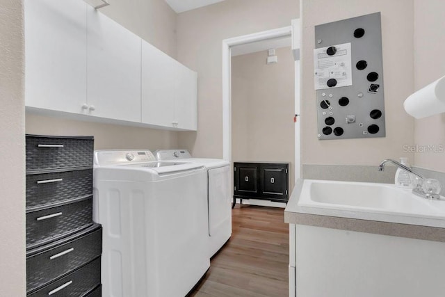 clothes washing area featuring washing machine and dryer, cabinet space, and light wood-style floors