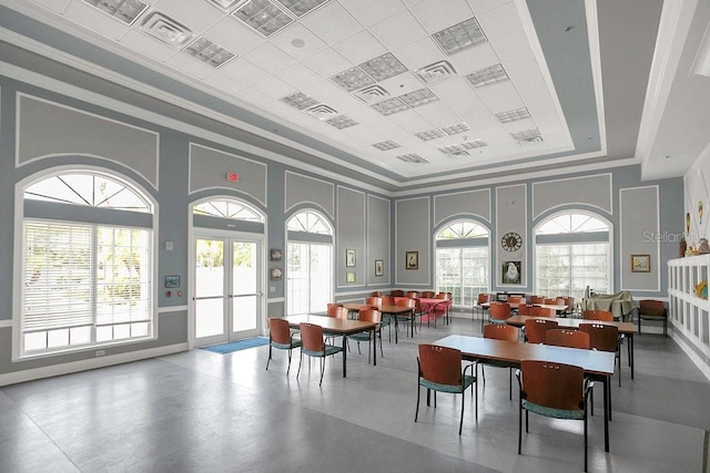 dining area featuring ornamental molding, a tray ceiling, a decorative wall, and french doors