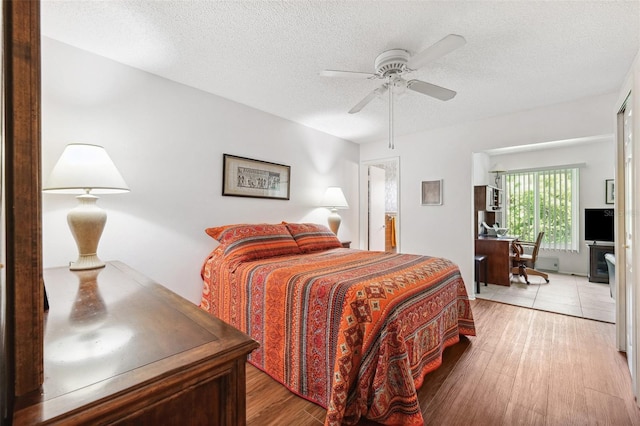 bedroom with light wood-type flooring, a textured ceiling, an office area, and a ceiling fan