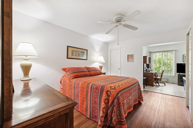 bedroom featuring light wood finished floors, a desk, a textured ceiling, and ceiling fan