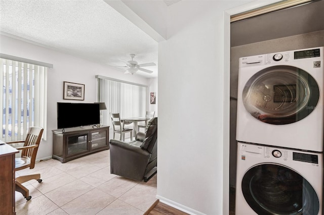 laundry room with stacked washer / dryer, ceiling fan, baseboards, light tile patterned floors, and a textured ceiling