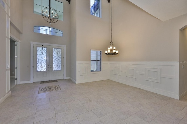 foyer entrance with a chandelier, a high ceiling, plenty of natural light, and a wainscoted wall