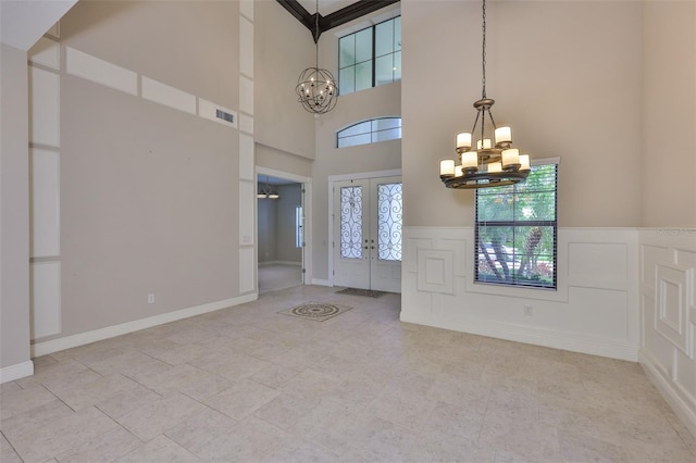 tiled foyer entrance featuring a chandelier, french doors, a towering ceiling, a decorative wall, and wainscoting