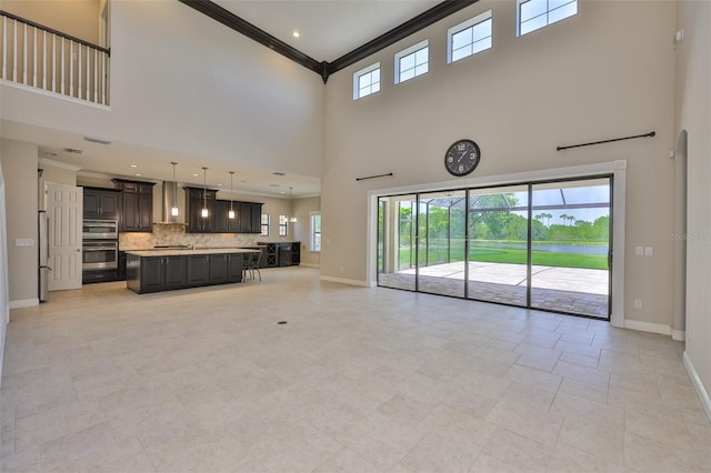 unfurnished living room with a towering ceiling, ornamental molding, and baseboards