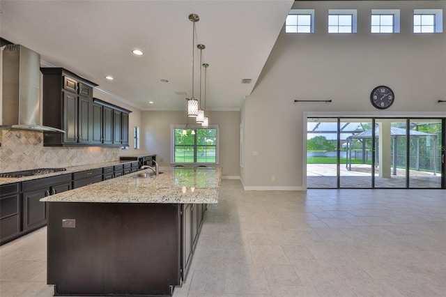 kitchen featuring wall chimney range hood, a sink, open floor plan, baseboards, and a kitchen island with sink