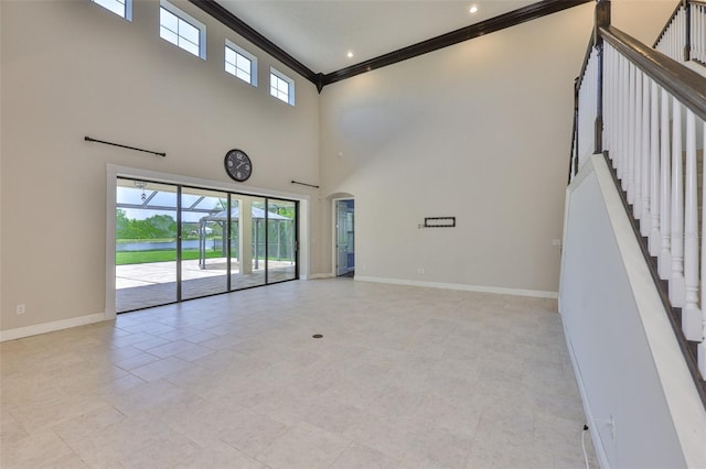 spare room featuring crown molding, baseboards, a towering ceiling, a water view, and stairway