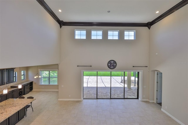 unfurnished living room with a towering ceiling, ornamental molding, baseboards, plenty of natural light, and light tile patterned flooring