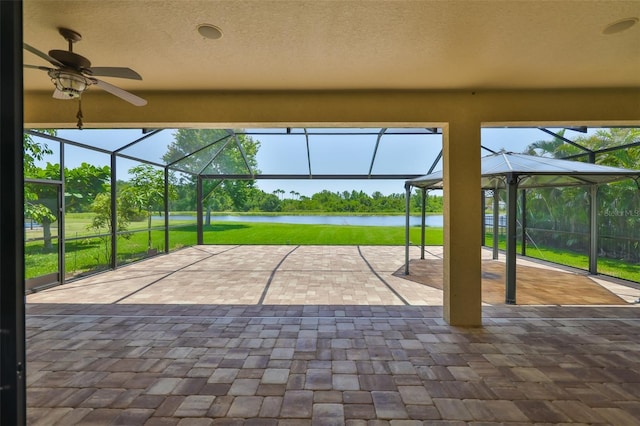 view of patio / terrace with a water view, glass enclosure, and ceiling fan