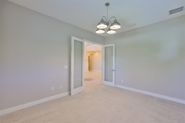 spare room featuring a chandelier, light colored carpet, baseboards, and french doors